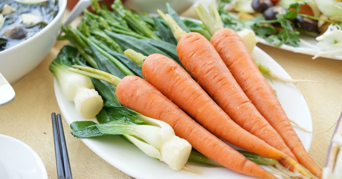 Présentation énergique de carottes fraîches et de légumes verts sur une table à manger.