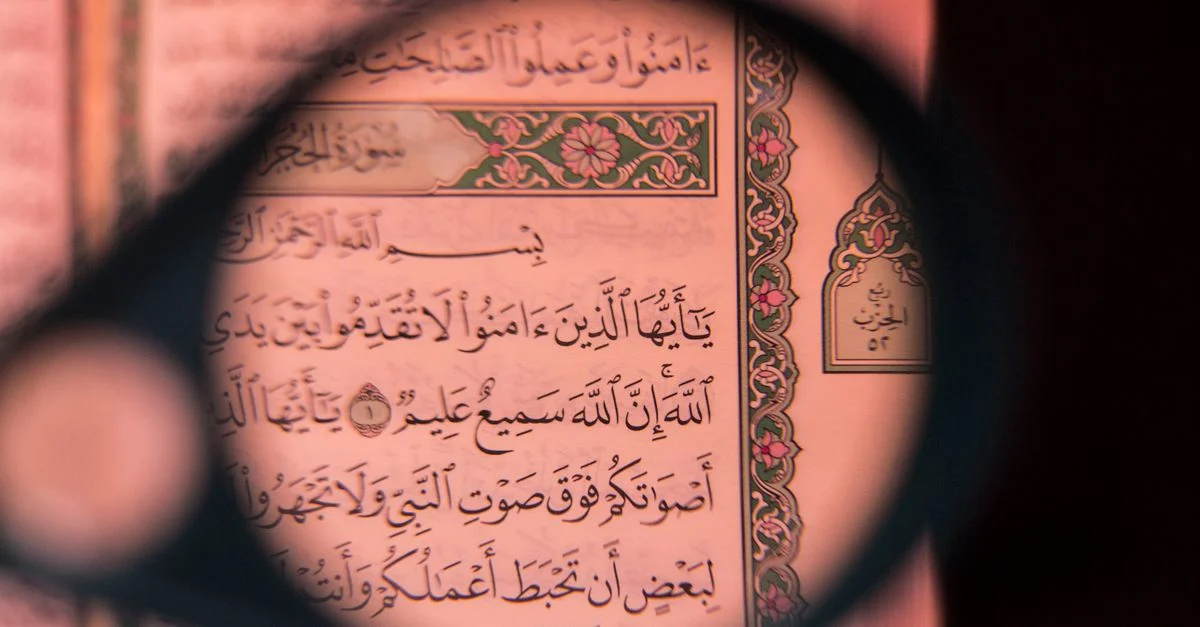 Détail d'une page du Coran observée à la loupe, mettant en évidence une calligraphie arabe complexe.
