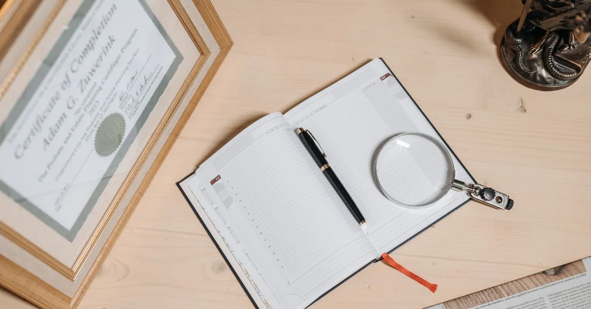 Un espace de travail bien rangé avec un certificat, un journal ouvert, une loupe et une statue sur un bureau en bois.