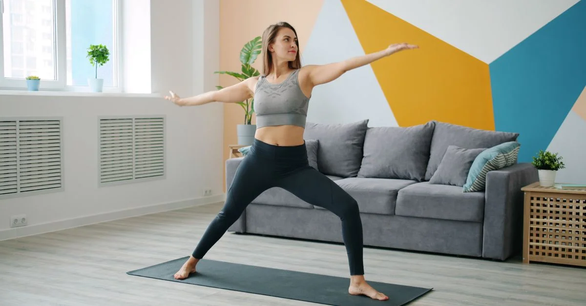 Femme en tenue de sport faisant du yoga dans le salon. Intérieur lumineux et moderne.