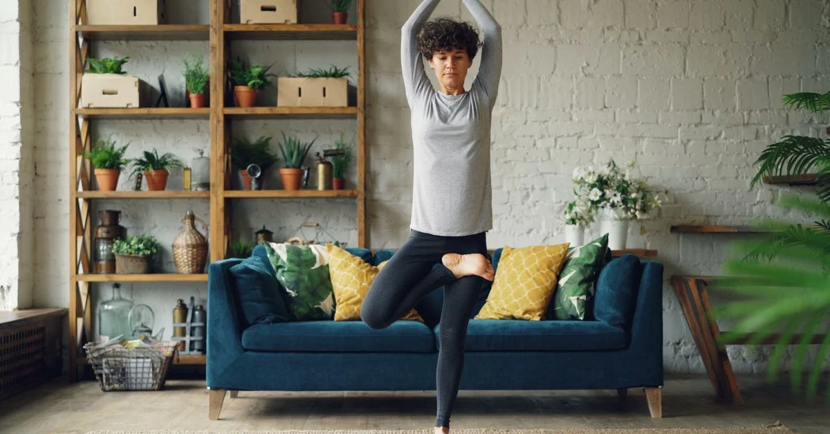 Femme faisant du yoga dans un salon moderne avec des plantes et une décoration confortable.